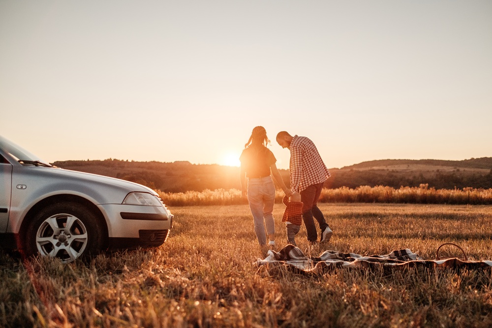 Glückliche junge Familie genießt ein Sommerwochenende-Picknick im Auto außerhalb der Stadt auf einer Wiese bei sonnigem Sonnenuntergang.